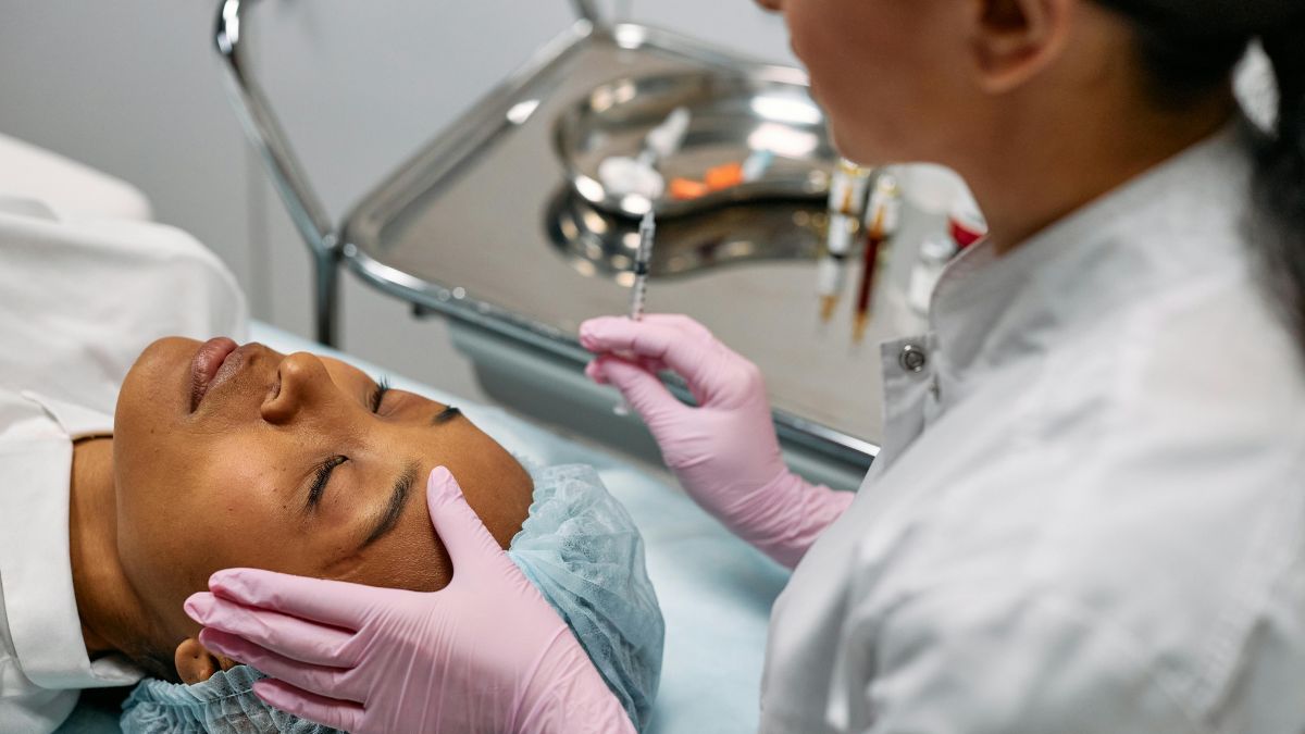 A woman receiving a facial treatment in a clinical setting, surrounded by medical equipment and a serene atmosphere.