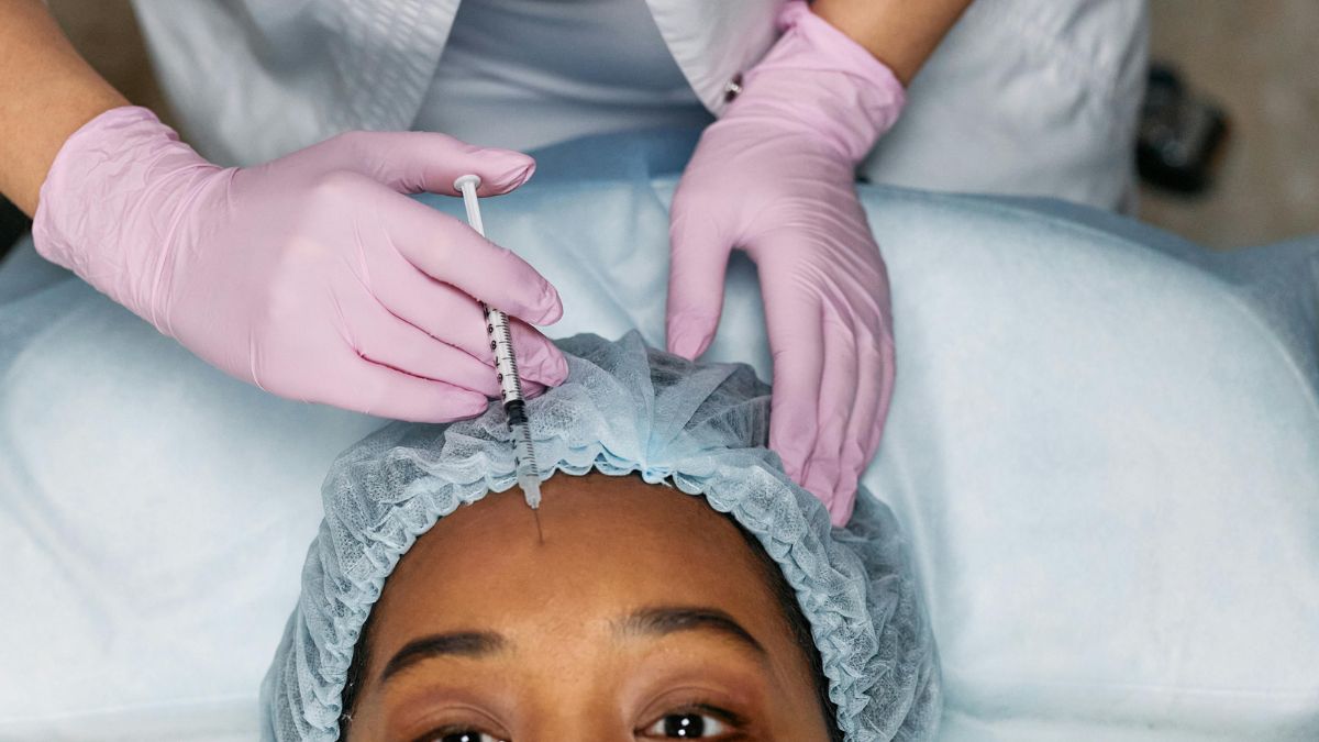 A woman lying in a clinic bed, having Botox Injections to Relief her headache by a professional.