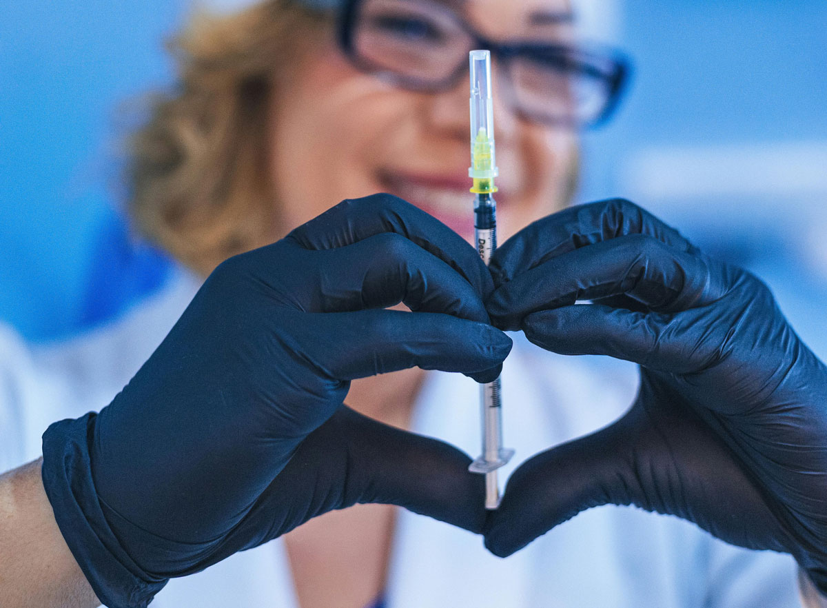 A woman in a white coat and black gloves holds a syringe, ready for a medical procedure or stem cell therapy injection