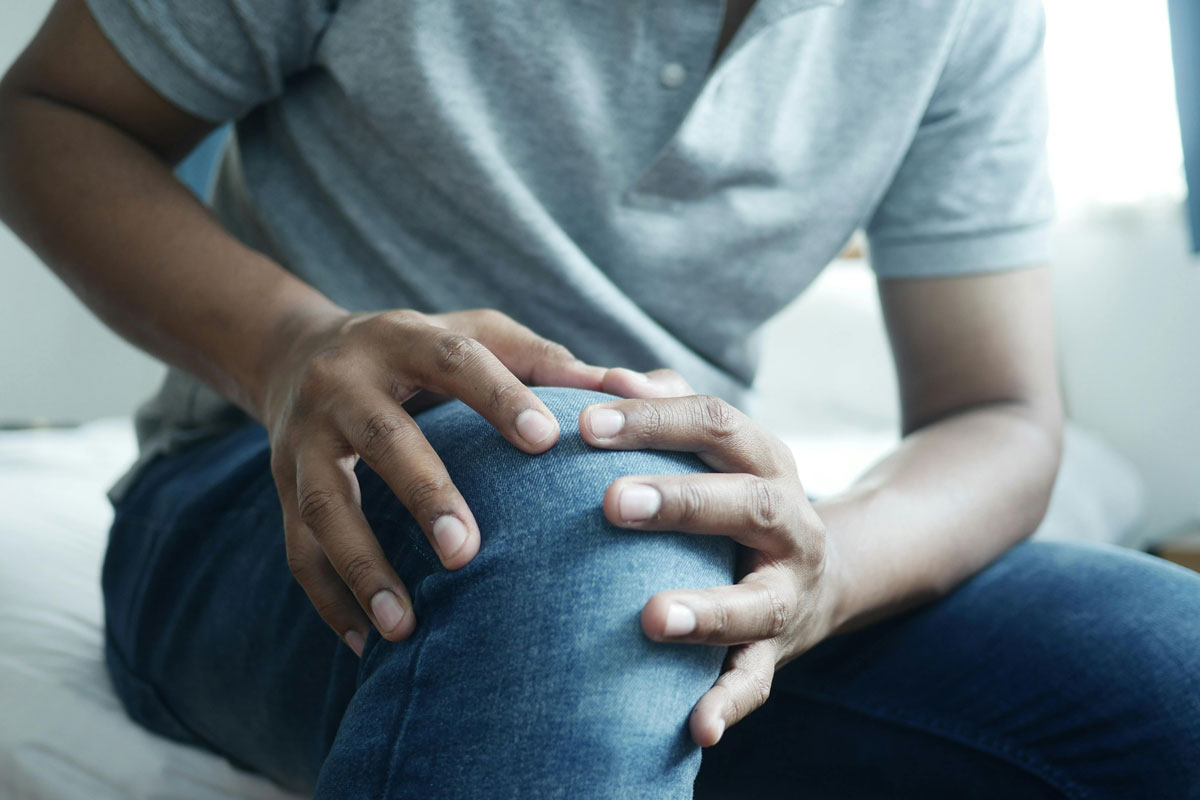 A man sitting on a bed, visibly experiencing discomfort due to knee pain