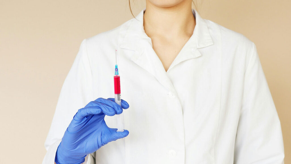 A woman in a lab coat confidently holds a syringe, ready for a medical procedure or vaccination