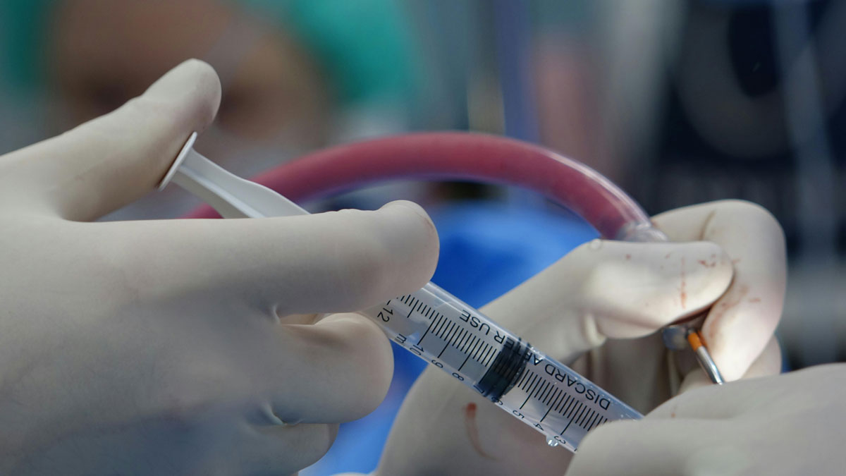 A healthcare professional in a surgical gown holds a syringe, ready for a medical procedure or stem cell therapy